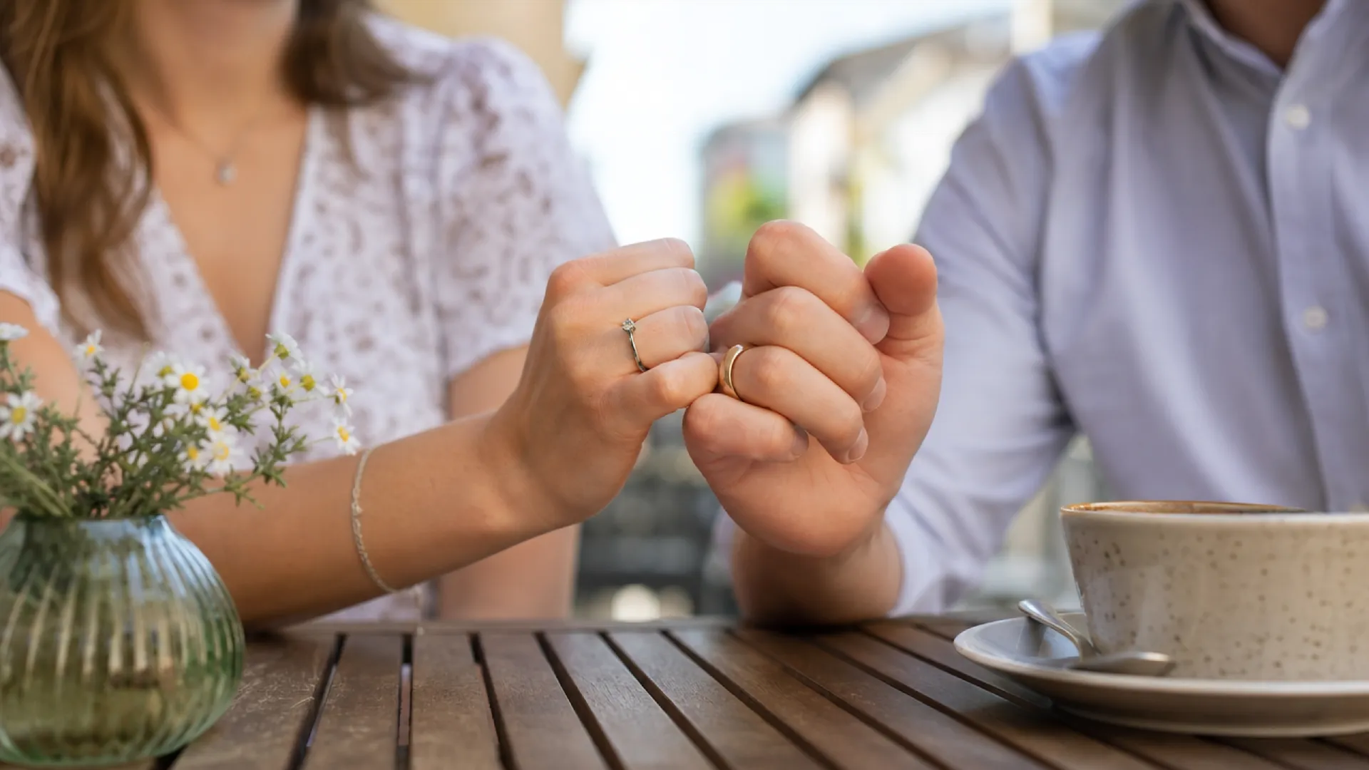 Zwei Personen, die sich mit den kleinen Fingern an einer Tischplatte festhalten, symbolisieren ein Versprechen oder eine Vereinbarung.